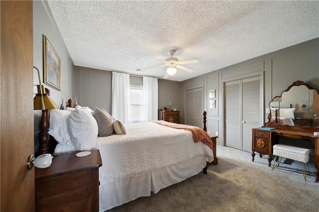 bedroom with ceiling fan, a textured ceiling, a decorative wall, carpet flooring, and two closets