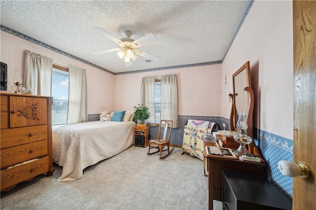 bedroom with a wainscoted wall, a textured ceiling, carpet flooring, and multiple windows