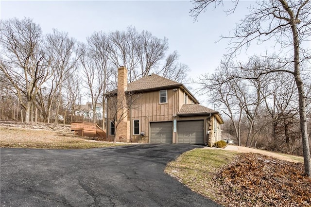 view of side of home featuring driveway, a garage, a chimney, and a shingled roof