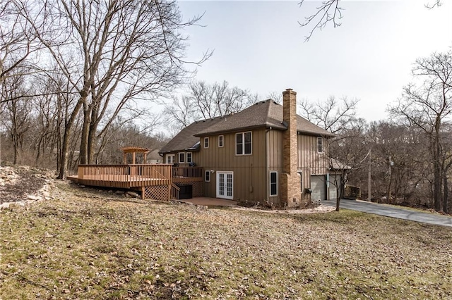 back of house featuring a garage, driveway, a chimney, a deck, and french doors