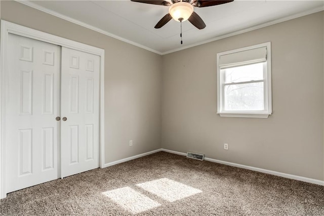 unfurnished bedroom featuring carpet floors, a closet, visible vents, ornamental molding, and baseboards