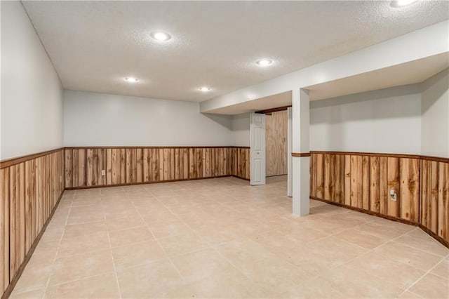 finished basement featuring a wainscoted wall, wood walls, and a textured ceiling