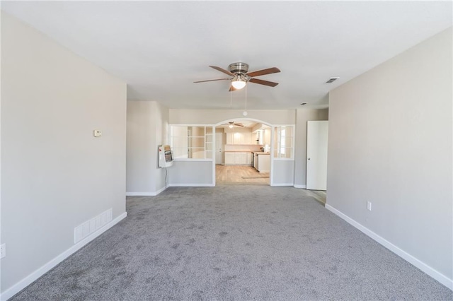 unfurnished living room with arched walkways, carpet, visible vents, a ceiling fan, and baseboards