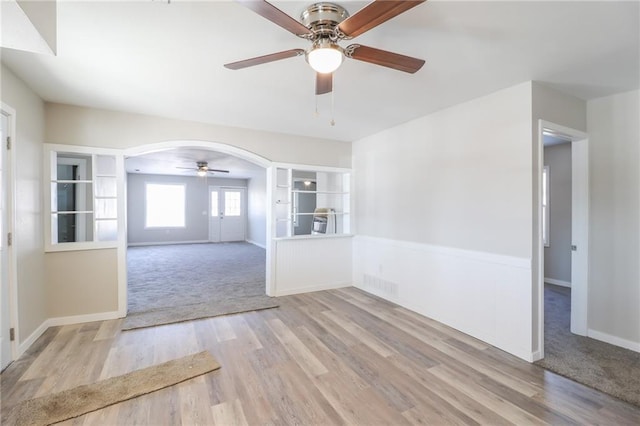 interior space featuring arched walkways, visible vents, ceiling fan, wood finished floors, and baseboards