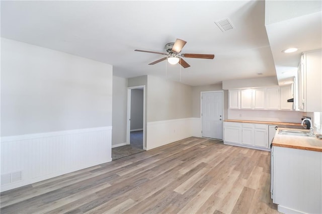 kitchen with a wainscoted wall, visible vents, a sink, and white cabinetry