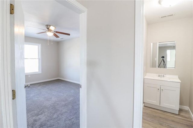 interior space with baseboards, visible vents, a ceiling fan, light colored carpet, and a sink