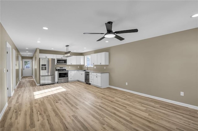 kitchen with appliances with stainless steel finishes, light wood-style floors, white cabinetry, a sink, and baseboards