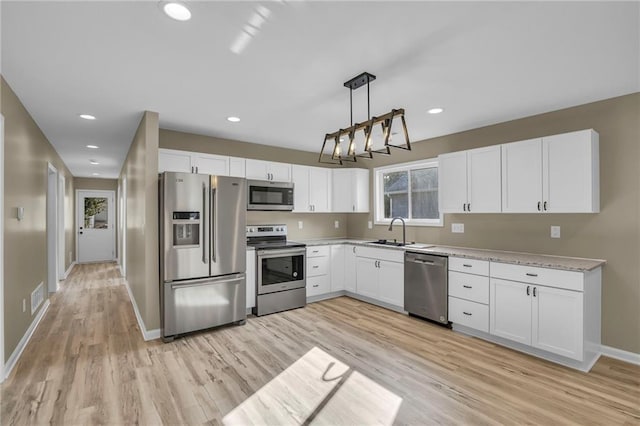 kitchen featuring light wood-style flooring, a sink, baseboards, white cabinets, and appliances with stainless steel finishes