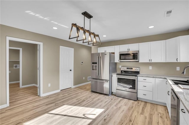 kitchen with light wood finished floors, appliances with stainless steel finishes, a sink, and white cabinets