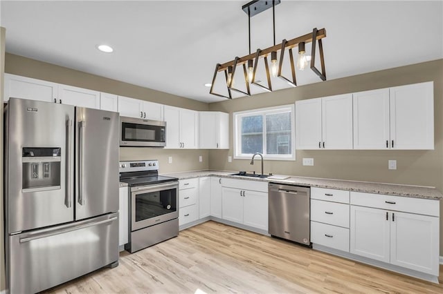 kitchen with stainless steel appliances, light wood-type flooring, white cabinets, and a sink