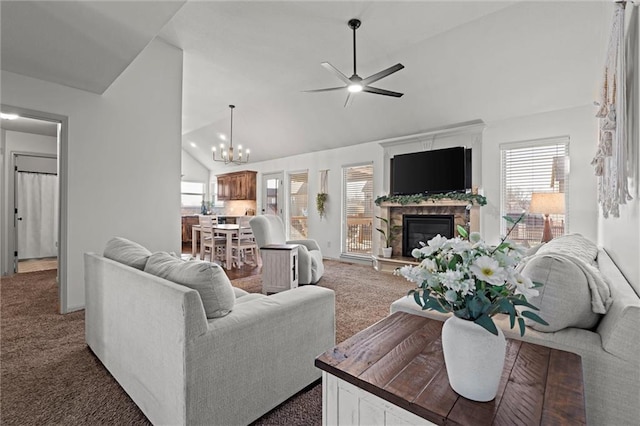 carpeted living room with a stone fireplace, ceiling fan with notable chandelier, and vaulted ceiling