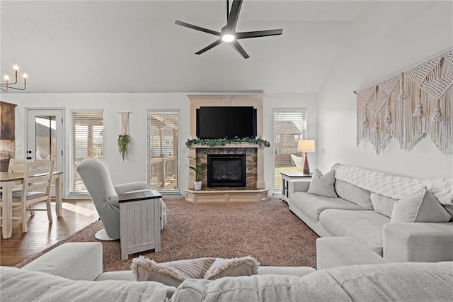 living area featuring ceiling fan with notable chandelier, lofted ceiling, a fireplace, and a wealth of natural light