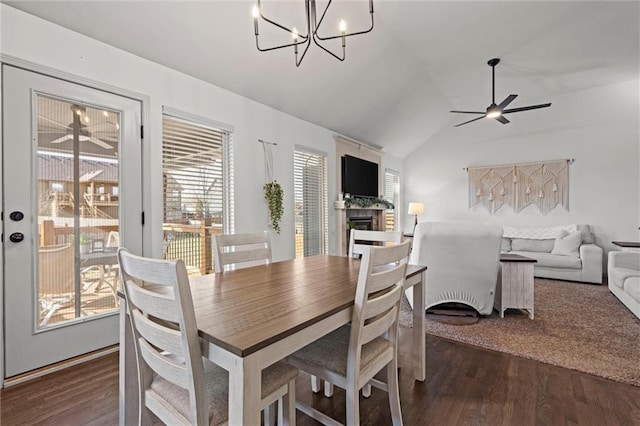 dining space featuring ceiling fan with notable chandelier, a fireplace, lofted ceiling, and wood finished floors