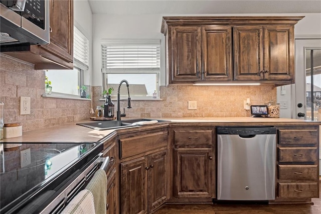 kitchen featuring tasteful backsplash, dark brown cabinets, light countertops, appliances with stainless steel finishes, and a sink