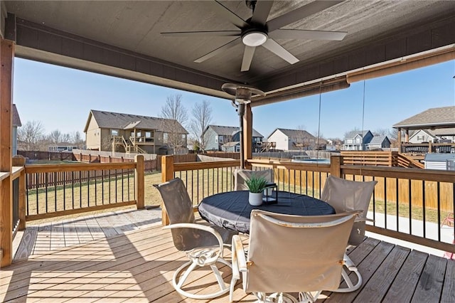 wooden deck featuring outdoor dining space, fence, ceiling fan, a lawn, and a residential view