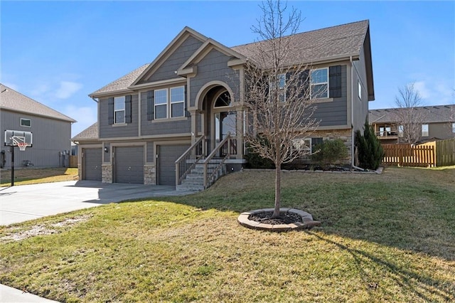 split foyer home featuring a front yard, fence, driveway, a garage, and stone siding