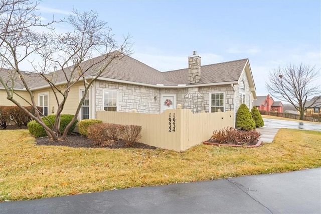 view of side of home with stone siding, a shingled roof, a chimney, and a yard