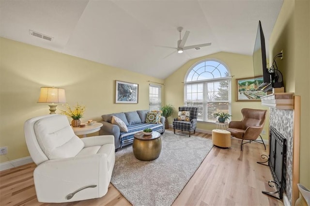 living area with visible vents, a ceiling fan, lofted ceiling, wood finished floors, and a fireplace