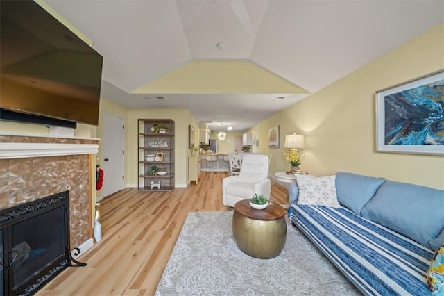 living room featuring lofted ceiling, light wood finished floors, a tiled fireplace, and baseboards