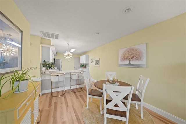 dining space featuring baseboards, visible vents, a notable chandelier, and light wood finished floors