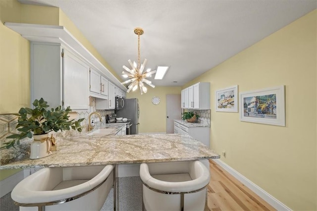 kitchen with a notable chandelier, light wood finished floors, decorative backsplash, appliances with stainless steel finishes, and a peninsula