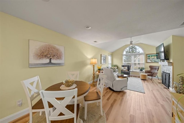 dining space with light wood-style flooring, a tiled fireplace, vaulted ceiling, ceiling fan, and baseboards