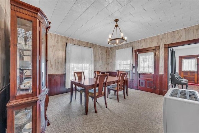 carpeted dining room with a notable chandelier, wainscoting, and wood walls