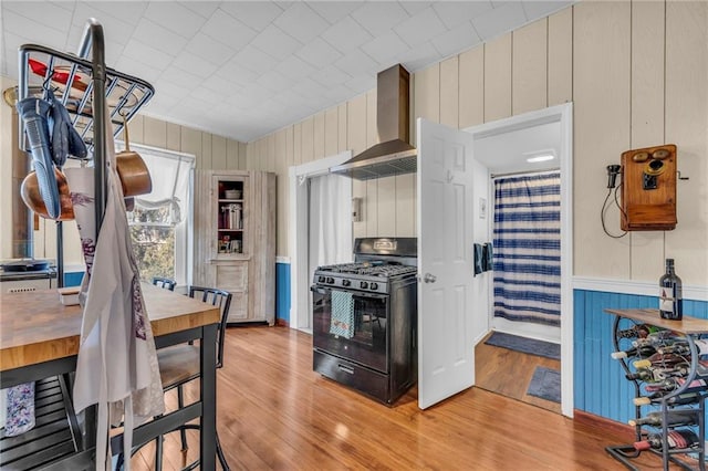 kitchen featuring wall chimney range hood, wooden walls, black range with gas cooktop, and light wood-style flooring