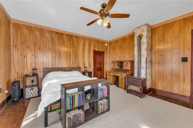 bedroom featuring wooden walls, a ceiling fan, a wood stove, and baseboards