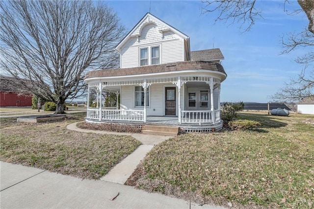 victorian house with roof with shingles, a porch, and a front yard