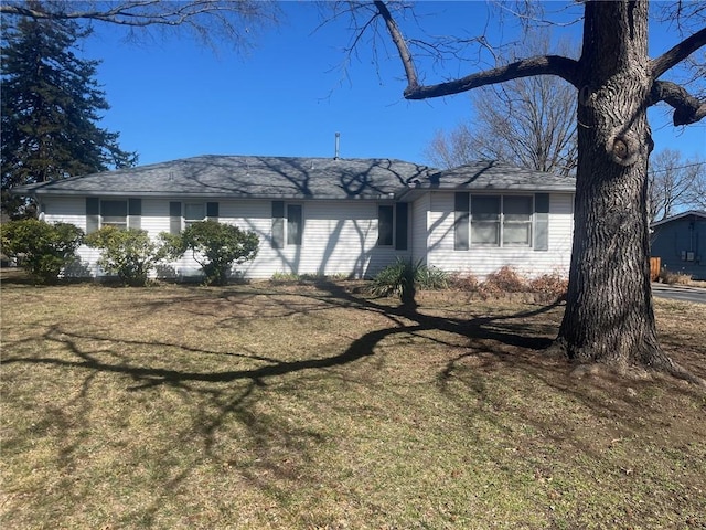 ranch-style home featuring roof with shingles and a front lawn