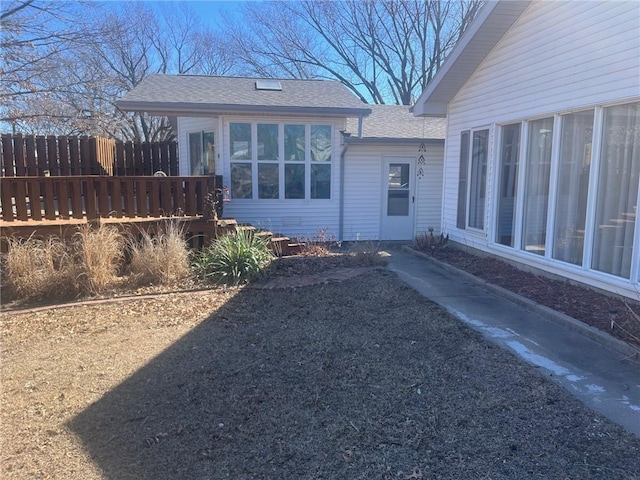 doorway to property featuring a shingled roof and fence