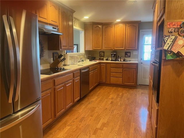 kitchen featuring under cabinet range hood, stainless steel appliances, a sink, light countertops, and light wood-type flooring