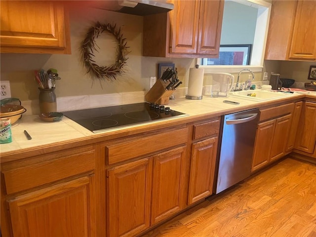 kitchen with light wood-style flooring, black electric cooktop, a sink, stainless steel dishwasher, and tile counters