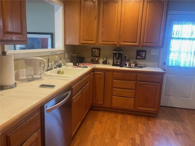 kitchen with light countertops, a sink, light wood finished floors, and stainless steel dishwasher