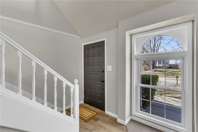 foyer entrance featuring baseboards, stairway, vaulted ceiling, light wood-style flooring, and a textured ceiling