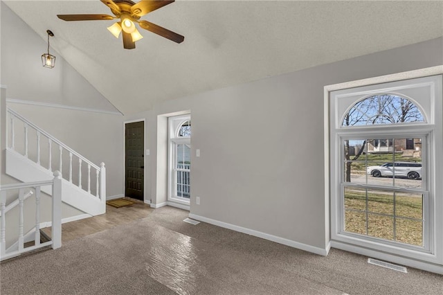 unfurnished living room with a ceiling fan, visible vents, baseboards, high vaulted ceiling, and stairs