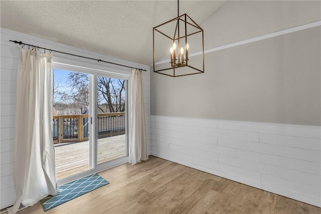 unfurnished dining area featuring an inviting chandelier, light wood-style floors, a wainscoted wall, and a textured ceiling