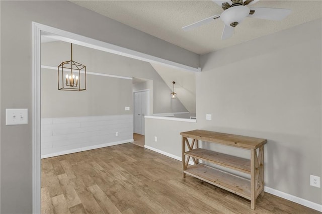 spare room with ceiling fan with notable chandelier, wood finished floors, baseboards, and a textured ceiling