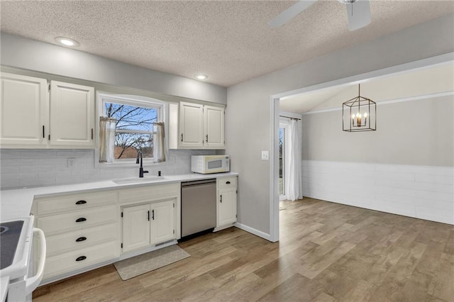 kitchen featuring white microwave, light wood-style flooring, stainless steel dishwasher, stove, and a sink