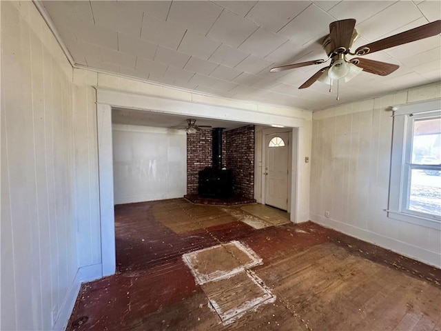 unfurnished living room featuring a wood stove and a ceiling fan