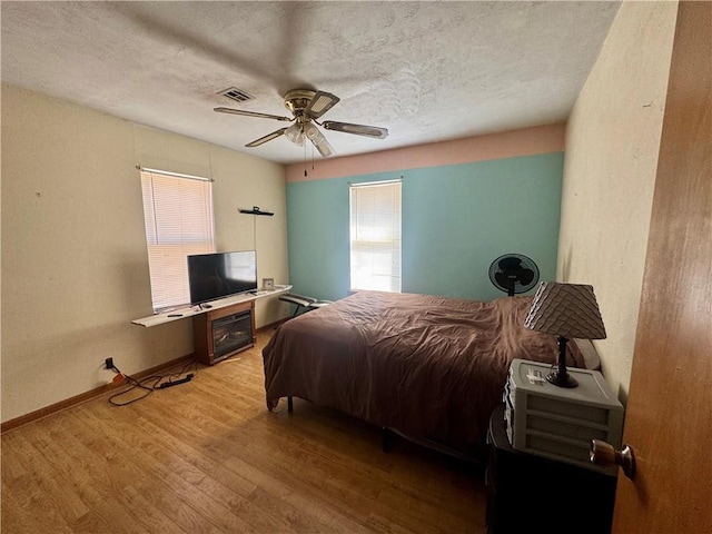 bedroom featuring a textured ceiling, wood finished floors, visible vents, baseboards, and a ceiling fan