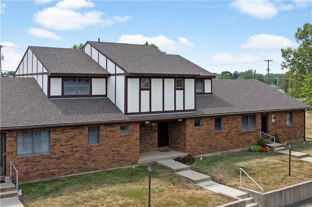 english style home featuring a front yard, roof with shingles, and brick siding