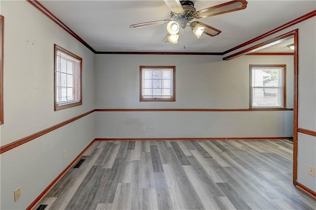 empty room with baseboards, visible vents, a ceiling fan, wood finished floors, and crown molding