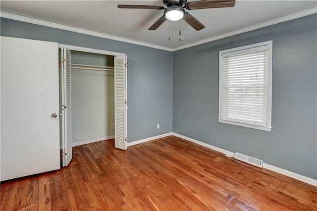 unfurnished bedroom with a closet, visible vents, ornamental molding, wood finished floors, and baseboards