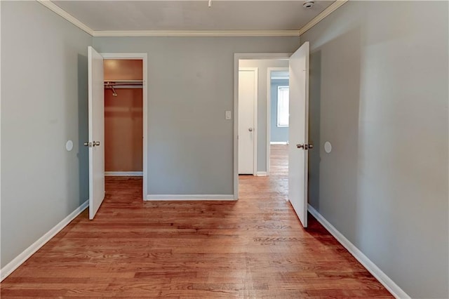 unfurnished bedroom featuring light wood-type flooring, a closet, baseboards, and crown molding