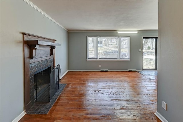 unfurnished living room featuring visible vents, ornamental molding, a brick fireplace, wood finished floors, and baseboards