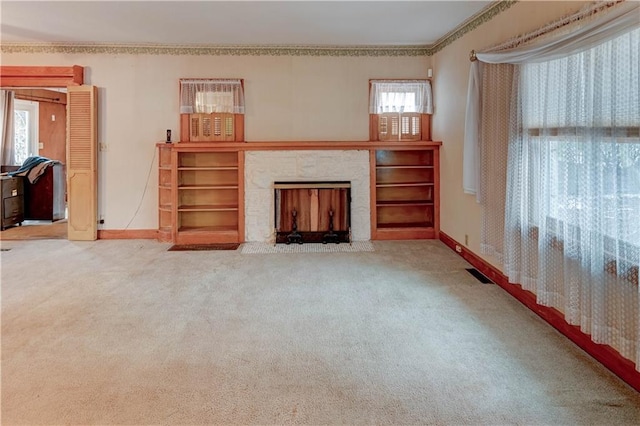 unfurnished living room with carpet floors, visible vents, plenty of natural light, and a fireplace with flush hearth