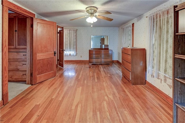 unfurnished bedroom featuring baseboards, a textured ceiling, light wood finished floors, and wallpapered walls