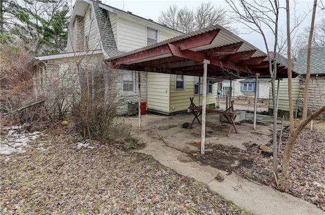 exterior space with stone siding, fence, a carport, and roof with shingles